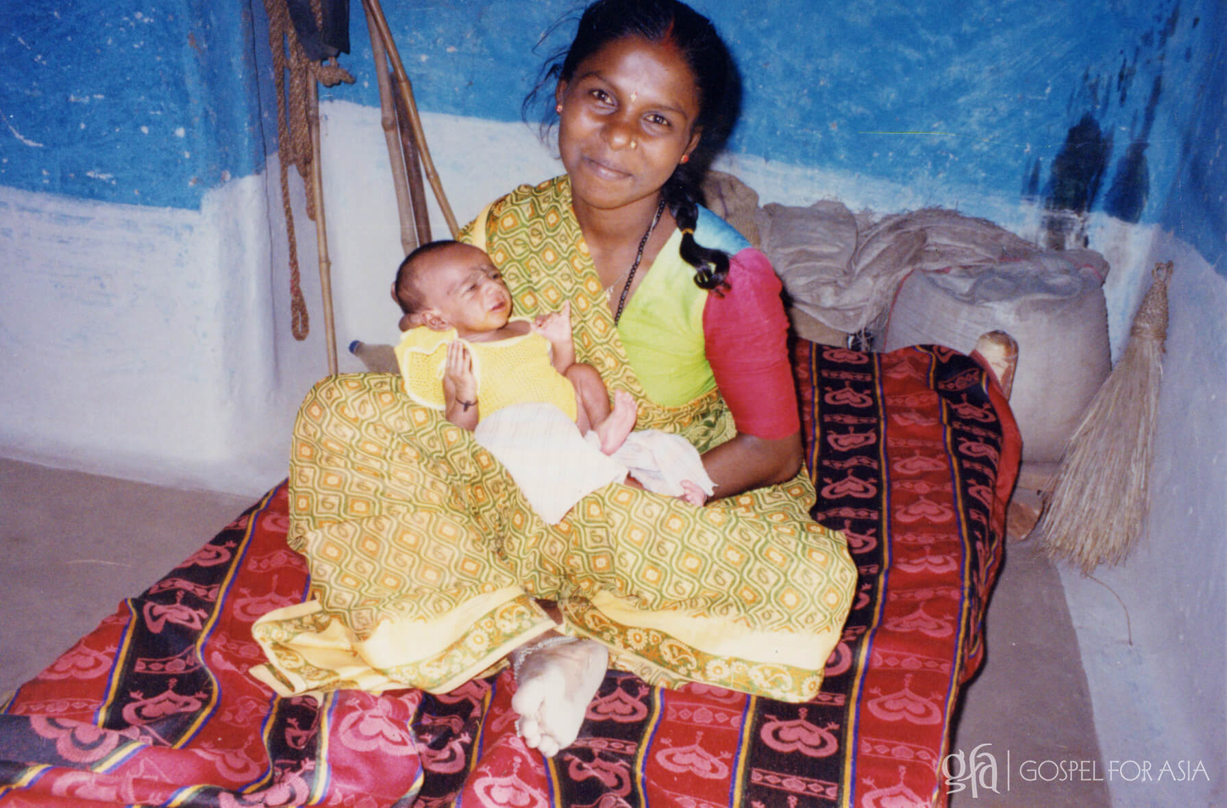 A young Indian woman happily poses with her newborn baby.