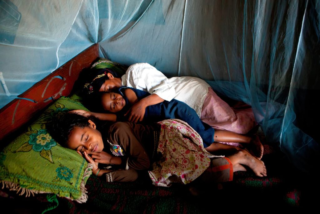 Family sleeping inside mosquito net covered bed.