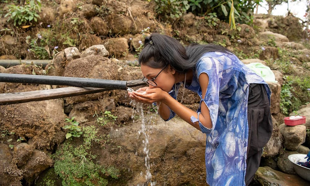 Girl drinking water from a pipe in Nepal